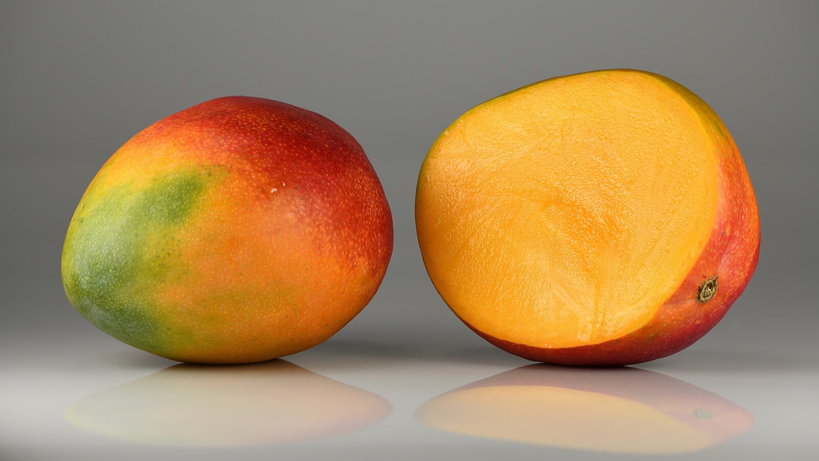 Whole and halved ripe mangoes on a plain background