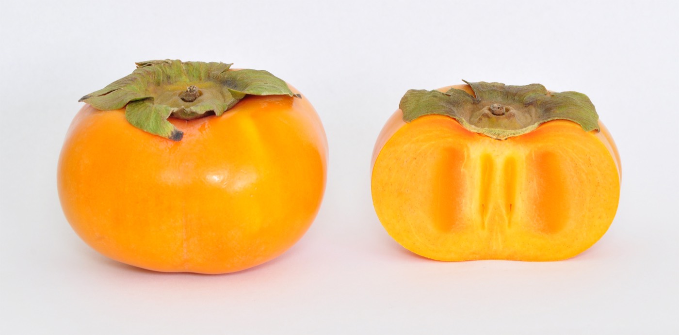 A ripe Fuyu persimmon on a plain background
